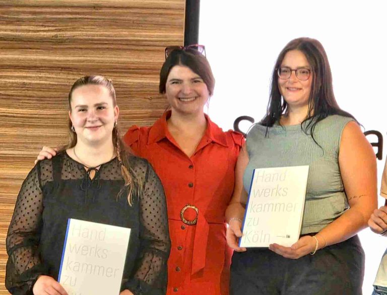 Sarah M. Rettig zusammen mit Lena und Michelle nach bestandener Gesellenprüfung. Drei Frauen posieren lächelnd mit Urkunden in der Hand bei einer Veranstaltungsfeier.