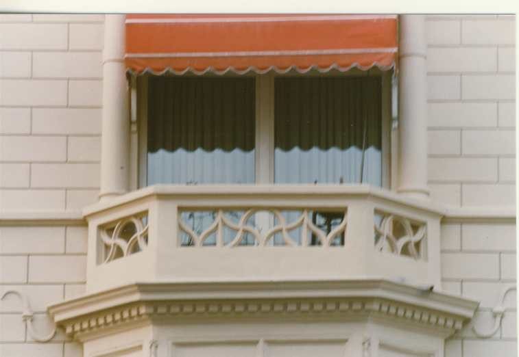 Fenster mit Balkon und dekorativem Geländer, orangefarbener Markise.