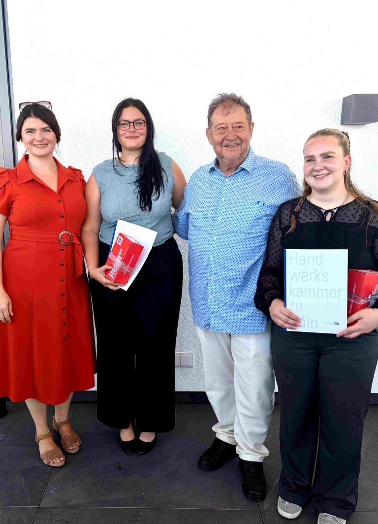 Sarah M. Rettig und Hans Hermann Hürth gratulieren Lena und Michelle zur bestandenen Gesellenprüfung. Vier Personen stehen zusammen, zwei halten Zertifikate, lächeln und stehen in einem hellen Raum.